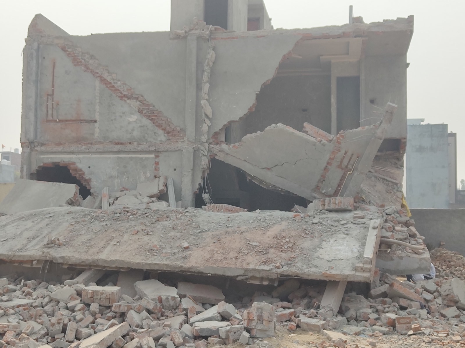 A concrete roof slab lying in one piece on the rubble of a demolished two-storey building