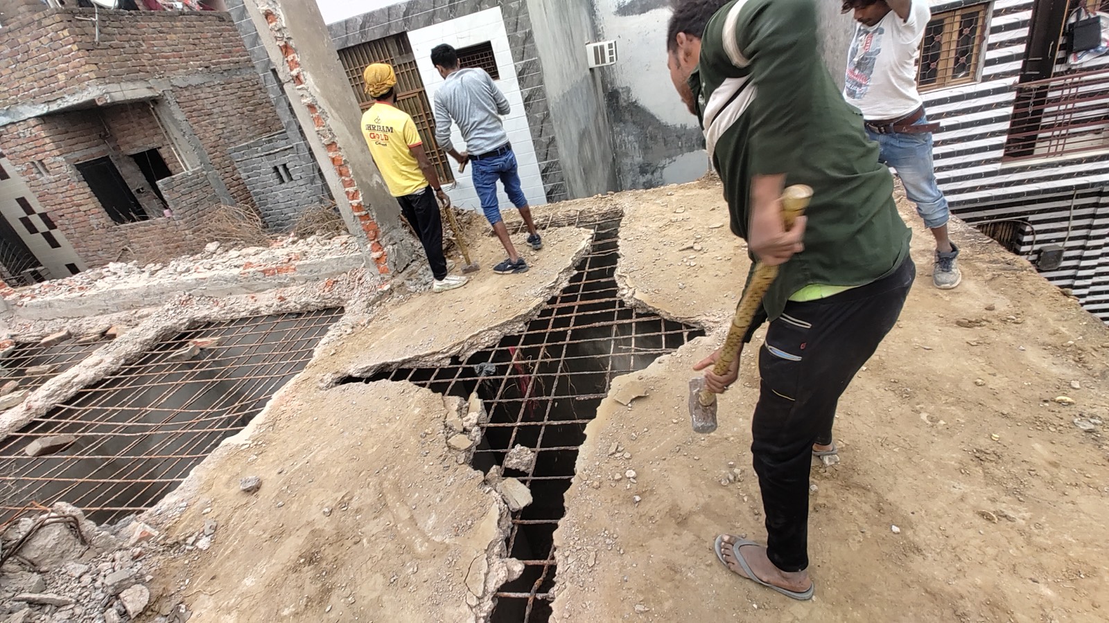 Workers breaking a concrete roof with hammers, exposing the steel mesh, between neighbouring houses